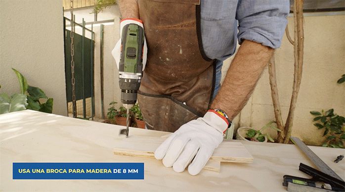 un hombre usa un taladro con broca para madera para hacer una perforación en un trozo de madera.