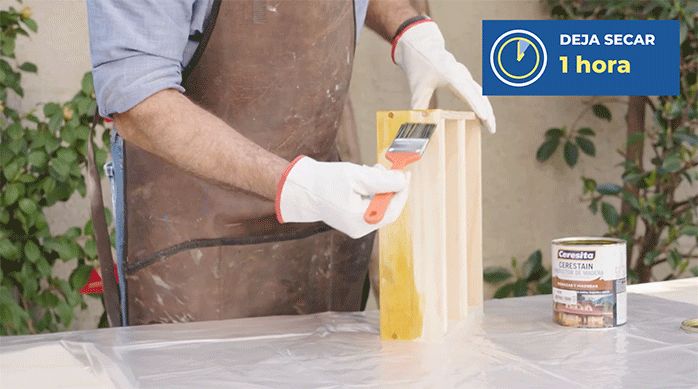 un hombre aplica barniz en la superficie del especiero colgante para proteger la madera.