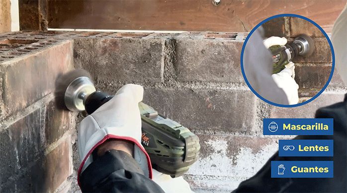 una persona con guantes de trabajo usa un cepillo metálico para limpiar el hollín del interior de un quincho.