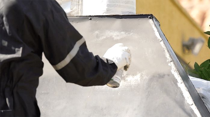 una persona aplica pintura resistente en spray resistente a altas temperaturas en la campana de un quincho.