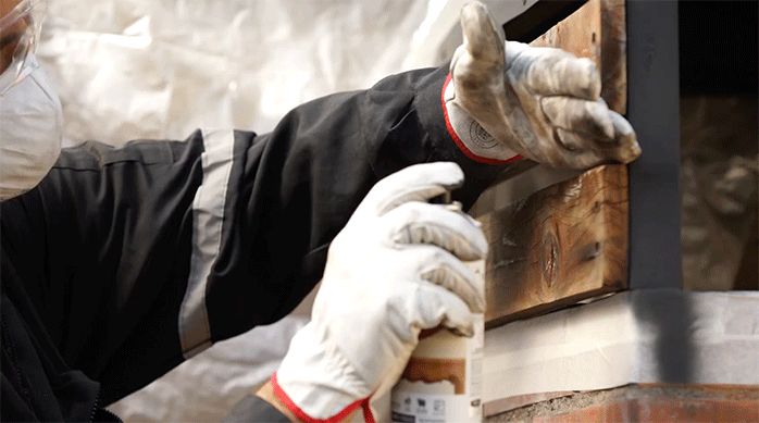 un hombre aplica barniz en spray en las maderas decorativas de un quincho.