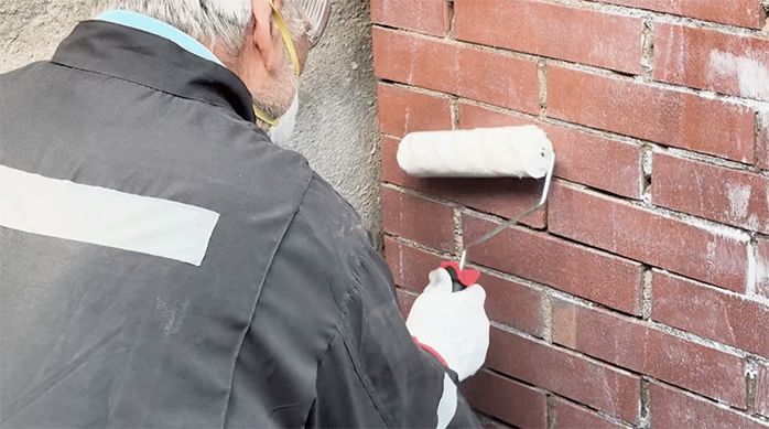 un hombre aplica sellador de superficies con un rodillo para proteger los ladrillos de un quincho.