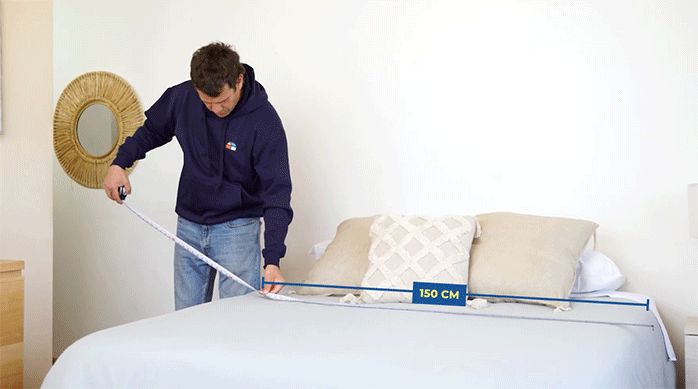 un hombre mide el ancho de una cama con una huincha para medir.