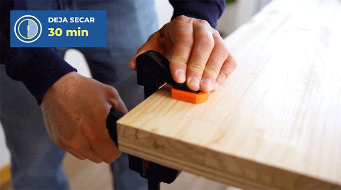 un hombre usa unas prensas para apretar una repisa laminada de madera a la base de terciado.