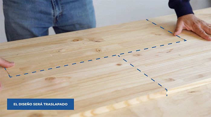 un hombre pega varias repisas laminadas de madera de forma traslapada en la base de terciado para construir el respaldo de cama.