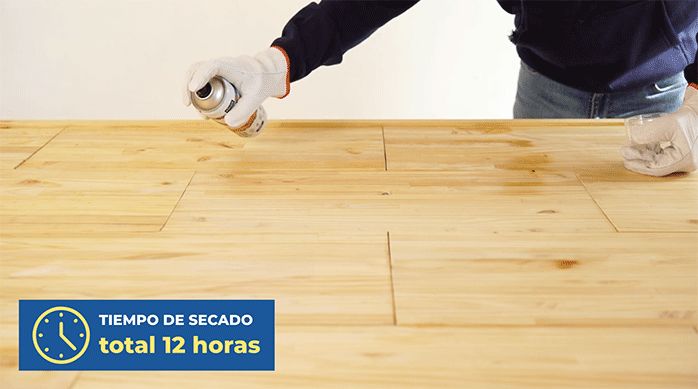 un hombre aplica barniz protector en spray en el respaldo de madera.