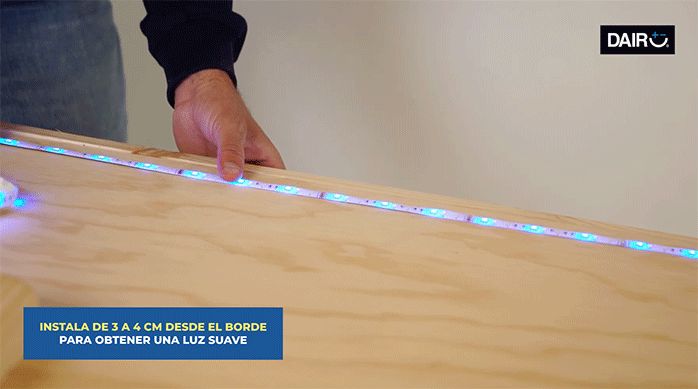 un hombre pega la cinta de luces led en la parte posterior del respaldo de madera para cama.