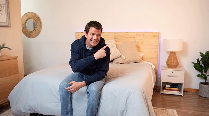 un hombre sentado sobre una cama e indicando su nuevo respaldo de madera con luces led.