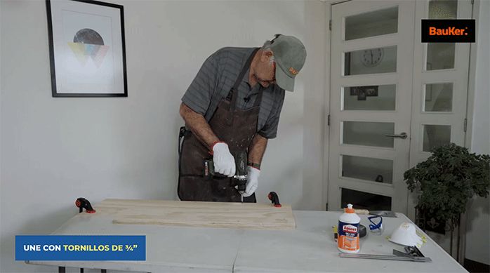 un hombre une dos trozos de madera usando tornillos.