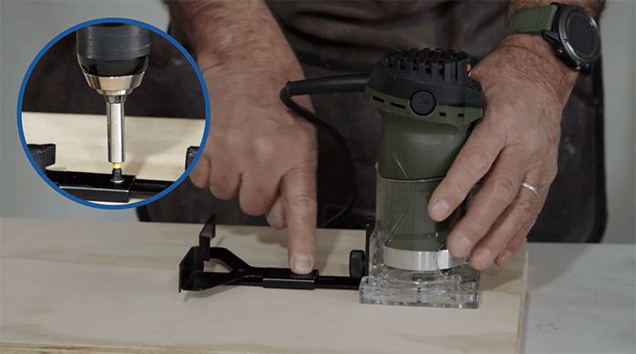 un hombre presenta la fresadora y su guía de corte sobre el trozo de madera y lo atornilla.