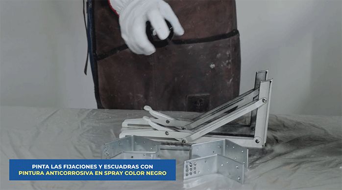 un hombre aplica pintura anticorrosiva en spray de color negro en las escuadras plegables.