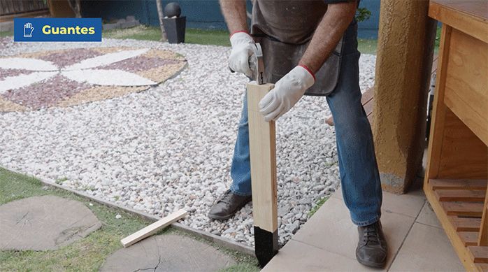 un hombre entierra una estacad de madera en el patio golpeando con un martillo.