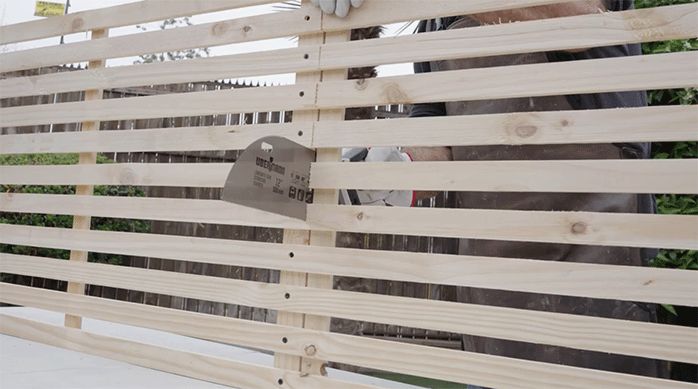una persona corta un enrejado de madera por la mitad usando un serrucho.