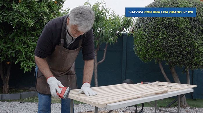 un hombre suaviza el corte en el enrejado de madera usando una lija y un soporte manual.