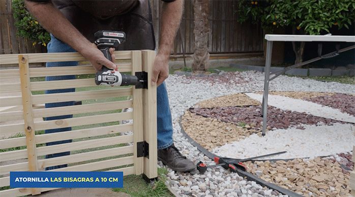 un hombre instala la puerta del enrejado de madera fijando las bisagras.