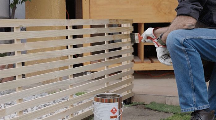 un hombre aplica stain en la superficie del enrejado de madera para protegerlo del ambiente.