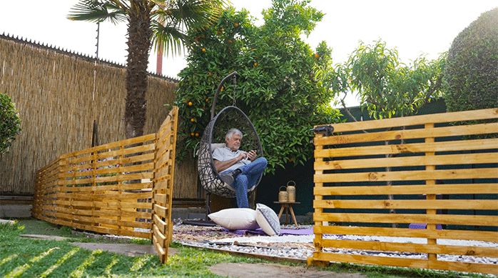 un hombre sentado en una silla colgante, sobre un jardín de piedras que fue separado del resto del jardín por un enrejado de madera.