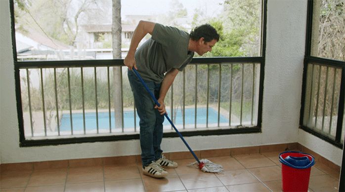 un hombre limpia el piso de un balcón con un trapero húmedo.