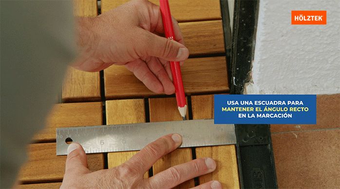 una persona marca una palmeta del deck de madera con una regla y lápiz para luego cortarla.