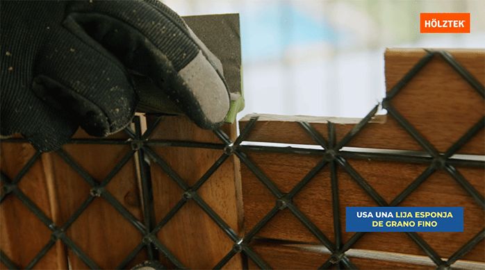 una persona usa una lija esponja de grano fino para suavizar una palmeta recién cortada del deck de madera.