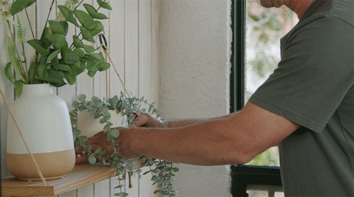 un hombre pone plantas en una repisa colgante en un balcón recién remodelado con deck de madera.