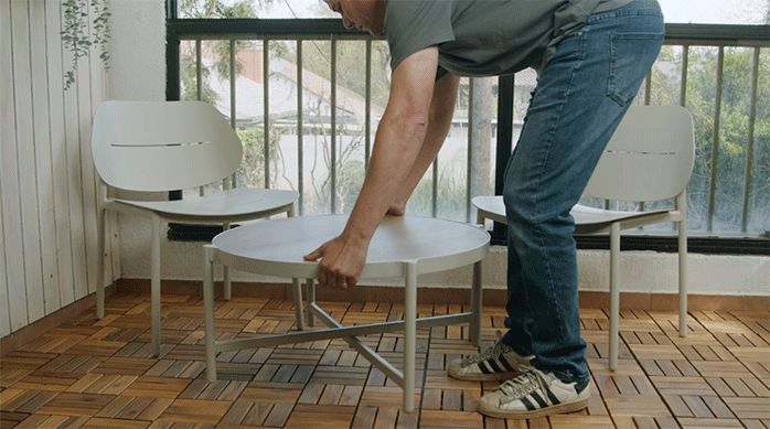 una persona pone una mesa de centro y dos sillas en el balcón recién remodelado con deck de madera.
