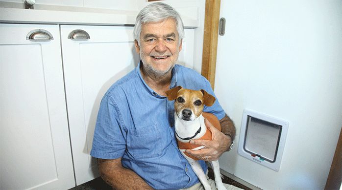 un hombre sostiene a un perro junto a una puerta para mascotas.