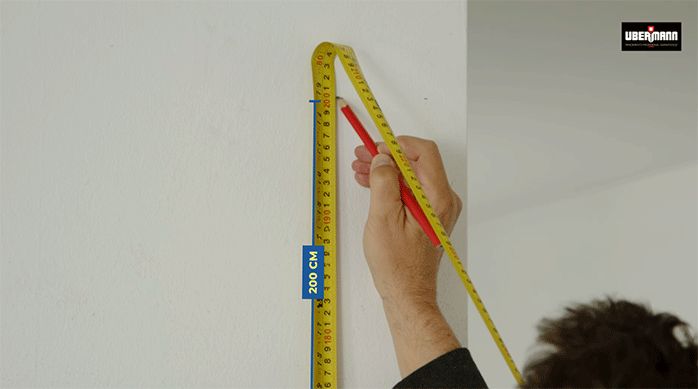un hombre marca 200 cm en un muro de cocina usando una huincha para medir y un lápiz.