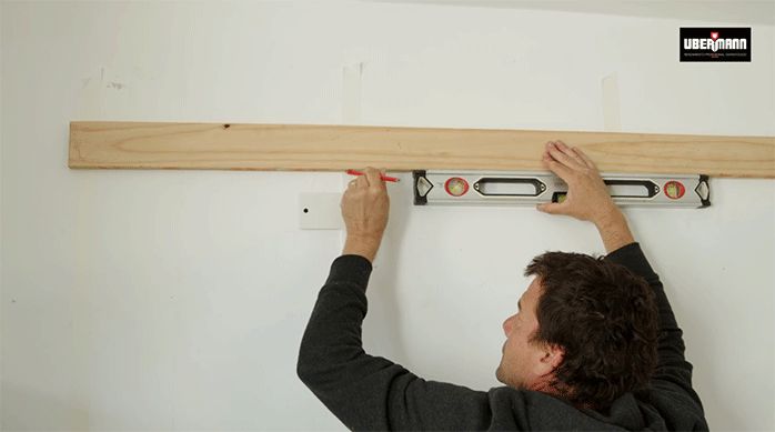 un hombre marca el lugar en que fijará el listón de madera en el muro de cocina usando el listón y un nivel de burbuja.