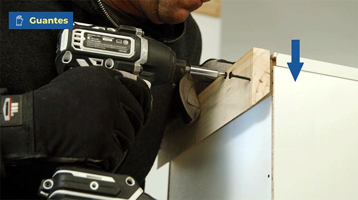 un hombre fija un trozo de madera en la parte posterior de un mueble modular de cocina usando tornillos.