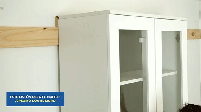 un hombre monta los muebles flotantes de cocina en la pared, haciendo calzar los listones de madera.
