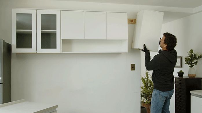 un hombre monta los muebles flotantes de cocina en la pared, haciendo calzar los listones de madera.