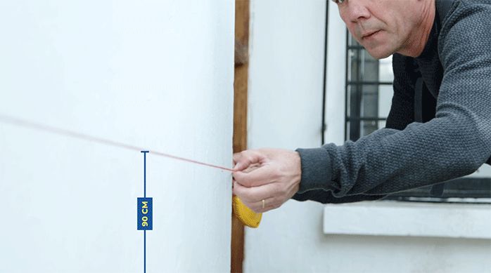 un hombre marca con un tizador 90 cm desde el piso en una fachada de casa.