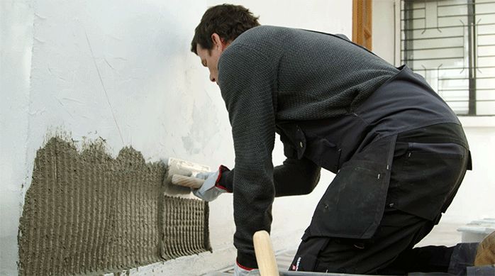 una persona aplica adhesivo para piedra y porcelanato en el muro de una fachada usando una llana dentada.