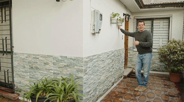 un hombre se apoya en el muro de una fachada recién remodelada con pintura y piedra natural.