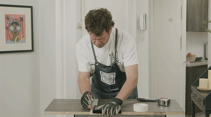un hombre marca la repisa de un mueble de cocina con cinta para enmascarar y un lápiz.