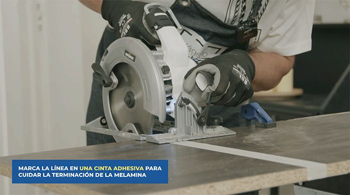 un hombre con guantes de seguridad corta la repisa del mueble de cocina usando una sierra circular.