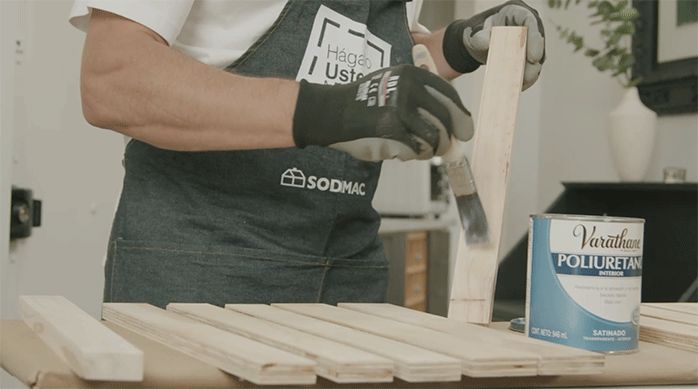 una persona aplica barniz poliuretano en un trozo de madera.