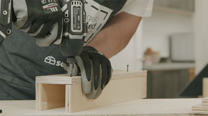 una persona fija el suple de madera usando tornillos y un desatornillador eléctrico.