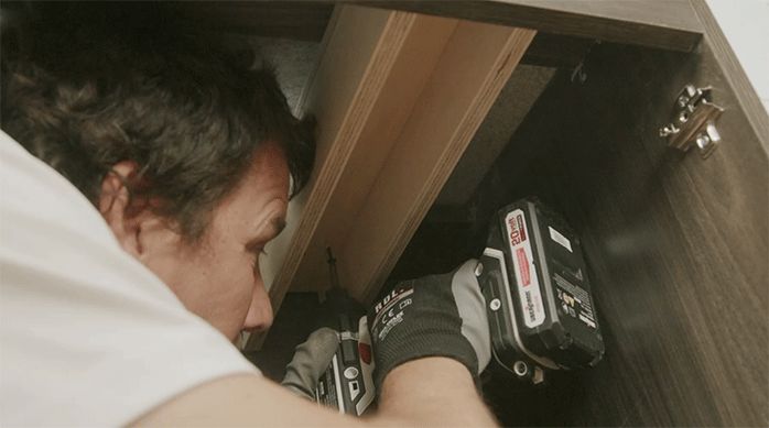 una persona instala un suple en un mueble de cocina usando tornillos.