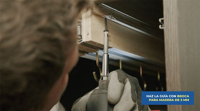 una persona fija las correderas en el mueble de cocina usando tornillos.