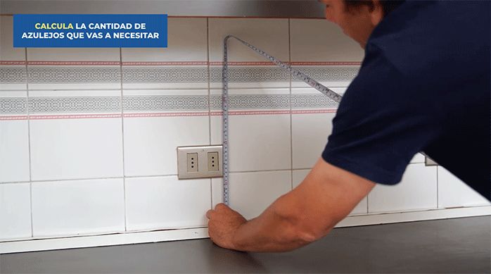 un hombre mide el alto de un muro de cocina con una huincha para medir.