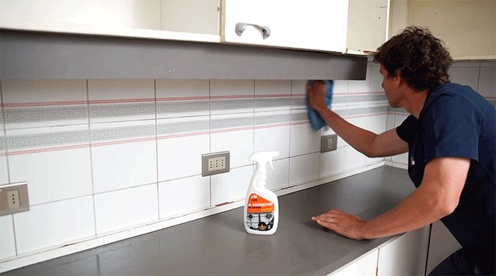 un hombre limpia un muro de cocina usando un paño y un producto antigrasa.