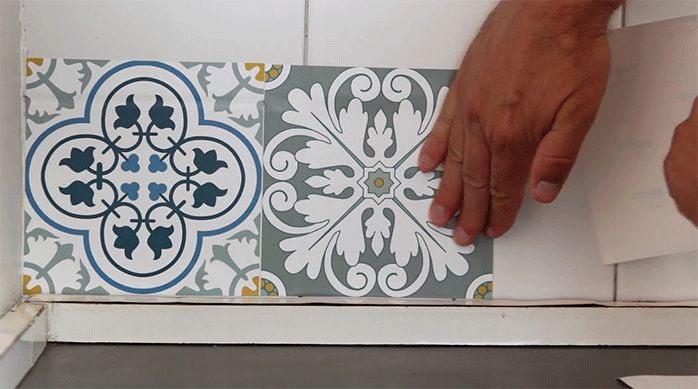 un hombre pega un mosaico adhesivo en un muro de cocina.
