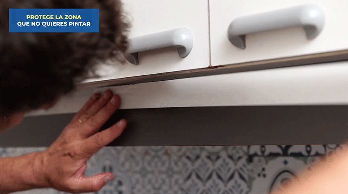 un hombre protege el borde de un mueble de cocina usando cinta para enmascarar.