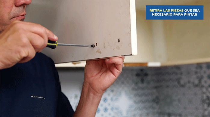 un hombre desatornilla las manillas de un mueble de cocina usando un desatornillador manual.