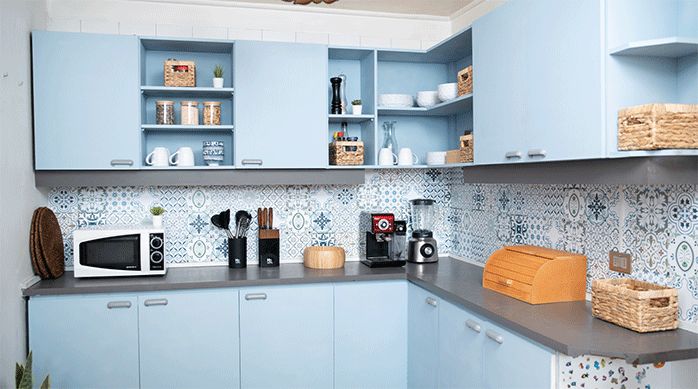 una cocina completamente renovada con pintura en spray color azul bebé, elementos de organización en varios sectores, mosaicos adhesivos en las paredes y luminarias led ultrafinas bajo los muebles.