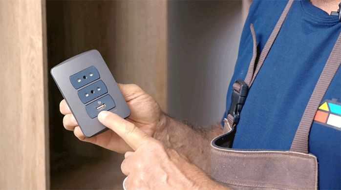 un hombre sostiene y muestra un enchufe de pared que incluye un puerto usb.
