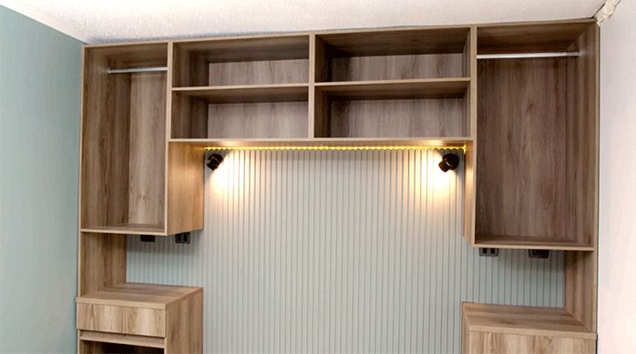 un clóset con veladores, percheros y cajones para la ropa, con revestimiento ranurado en su respaldo y luces led.