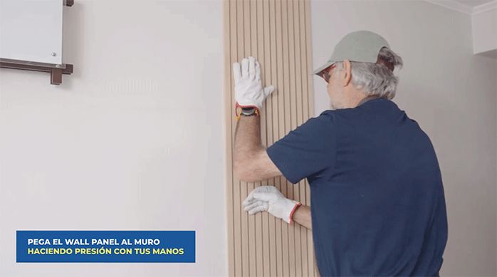 un hombre presiona la plancha de wall panel en la pared para pegarla.